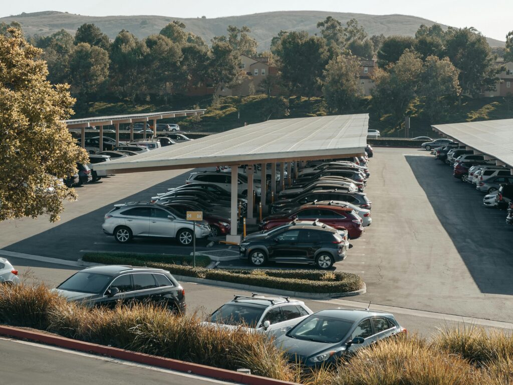 View of a large parking lot with solar panel shades and diverse vehicles parked.